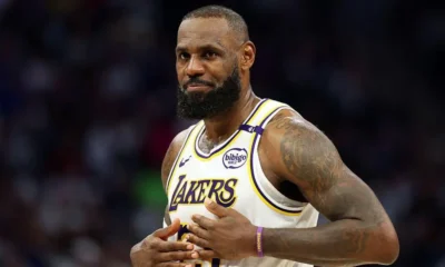 LeBron James sitting courtside in Lakers warm-up gear after being ruled out with sciatica.