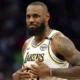 LeBron James sitting courtside in Lakers warm-up gear after being ruled out with sciatica.