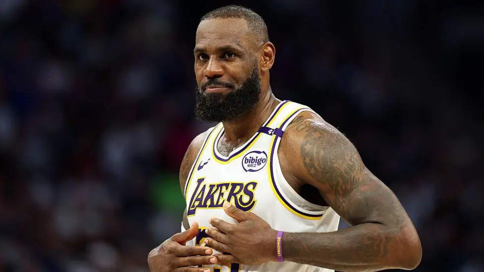 LeBron James sitting courtside in Lakers warm-up gear after being ruled out with sciatica.