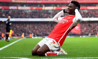 Bukayo Saka celebrating a goal with Arsenal teammates.