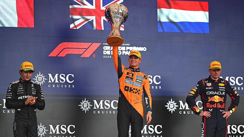 Racing Bulls team member making a thumbs-down gesture during Lando Norris’ Sao Paulo Grand Prix trophy celebration.