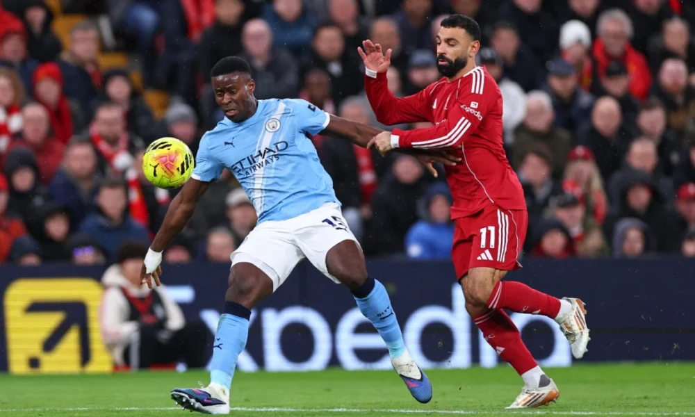 Marc Guehi in action for Manchester City at Anfield as Liverpool fans react during Premier League clash.