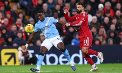 Marc Guehi in action for Manchester City at Anfield as Liverpool fans react during Premier League clash.